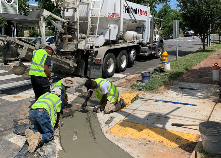 A Cemen Tech volumetric mixer sits behind workers hand screeding a newly placed ADA-accessible concrete curb in Raleigh, NC.