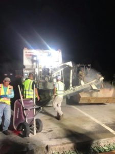 A volumetric concrete mixer pours concrete into a skidsteer bucket at night along I-95 near Roanoke Rapids, NC.