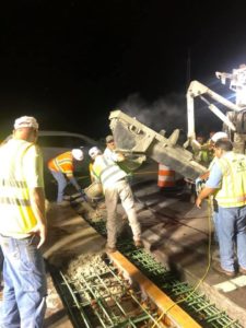 Crews look on as a concrete finisher places concrete into an I-95 bridge joint at night.