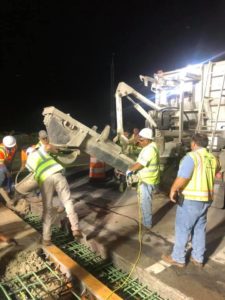Crews look on as a concrete finisher places concrete into an I-95 bridge joint at night.