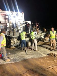 Workers clean out the chute of a volumetric concrete mixer at night.
