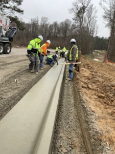 3 concrete workers look on as another kneels next to a new concrete curb in Wendell, NC.