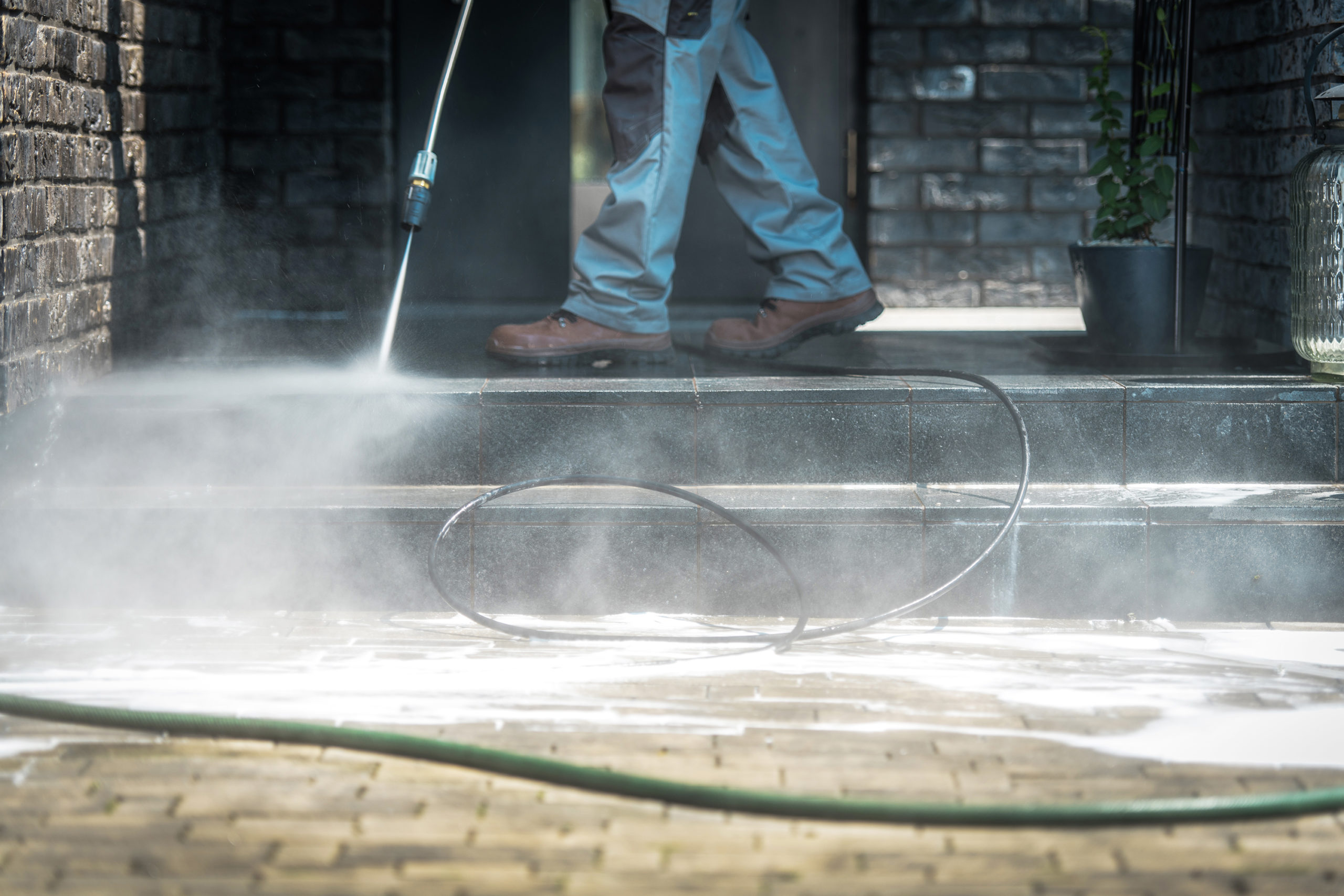 A man uses a pressure washer to clean concrete steps in front of a home.